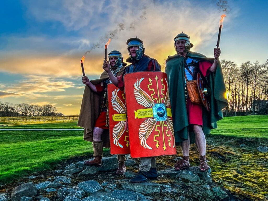 Hadrian's Wall Guide. Three men dressed as roman centurions hold flaming torches aloft.